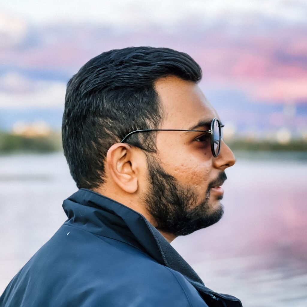 Bearded man in sunglasses gazing at sunset over tranquil lake, showcasing serene and thoughtful atmosphere.
